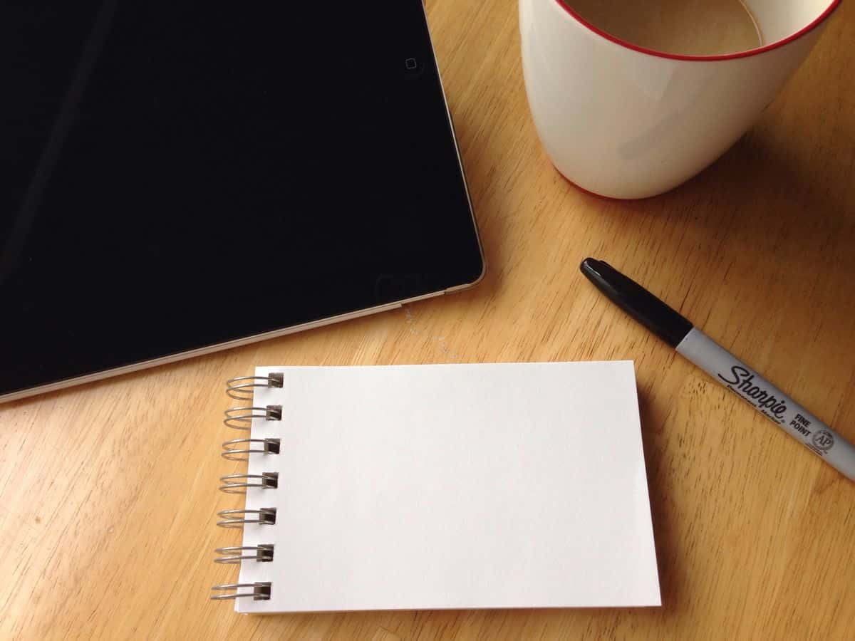 A close-up of a small notepad, marker, tablet computer and coffee on a desk. For initial brainstorming, a pen and paper may be your best UX design tools.