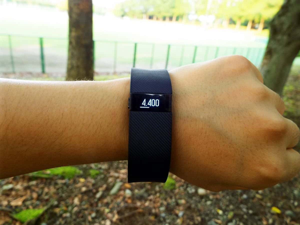 A close-up of a person’s arm, a dark purple FitBit around the wrist displaying a step count of 4,400.