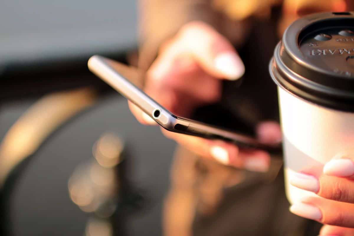 A close-up of a woman’s hand holding a smartphone, a cup of coffee in her other hand.
