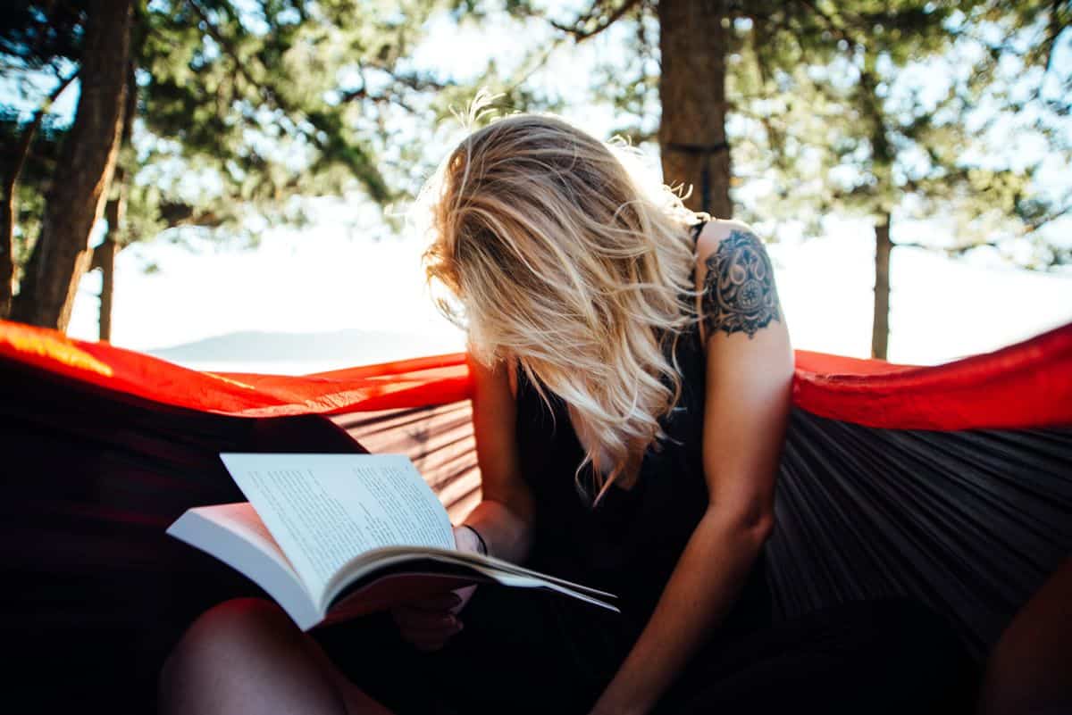 A young woman sitting in a hammock burying her head in a book.