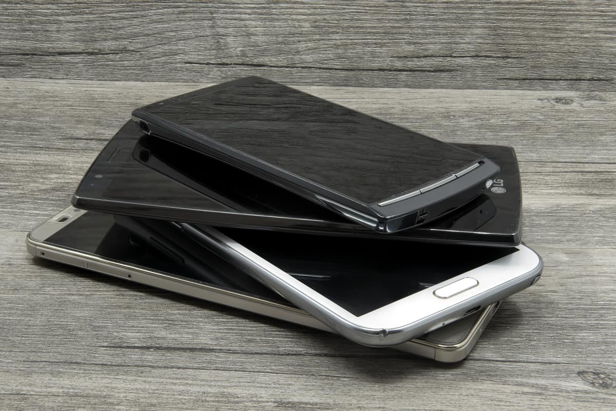 A stack of mobile devices — some old, some new — sits on a grey wooden table, awaiting mobile usability testing.