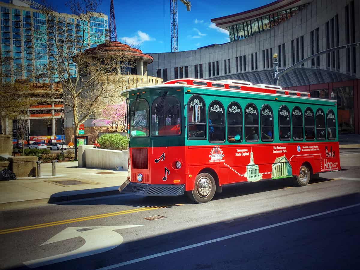 A red and green trolley drives through a peaceful city street.