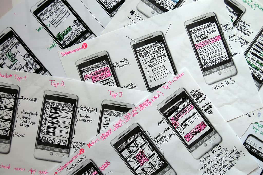 Image of a pile of mobile template papers filled with wireframes created with black and pink pens.