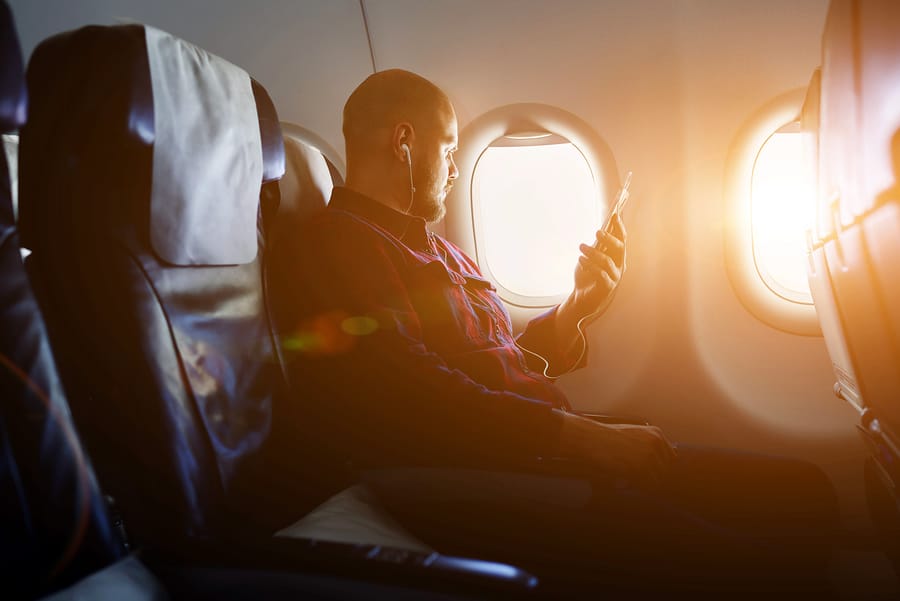 A photo of a man sitting on a plane, listening to something on his phone through earbuds.