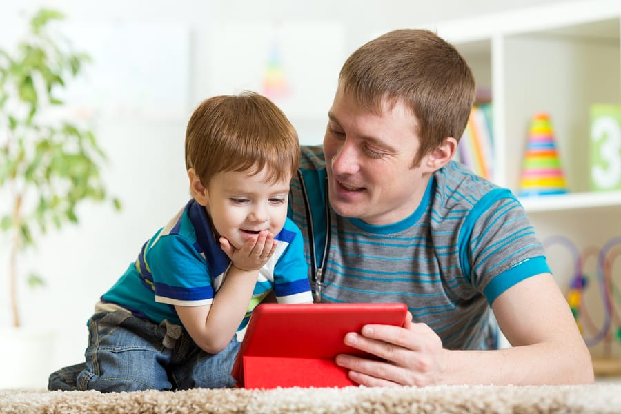 A photo of a father and son playing a game on a tablet.