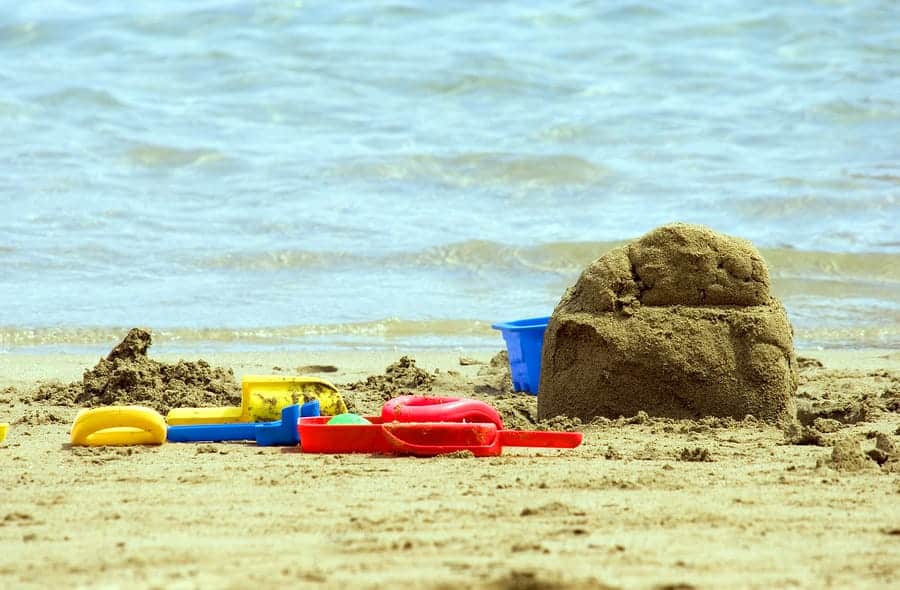 A photo of an unfinished sand castle surrounded by plastic tools and buckets.