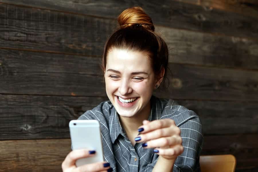 A photo of a woman smiling broadly at a message on her iPhone.