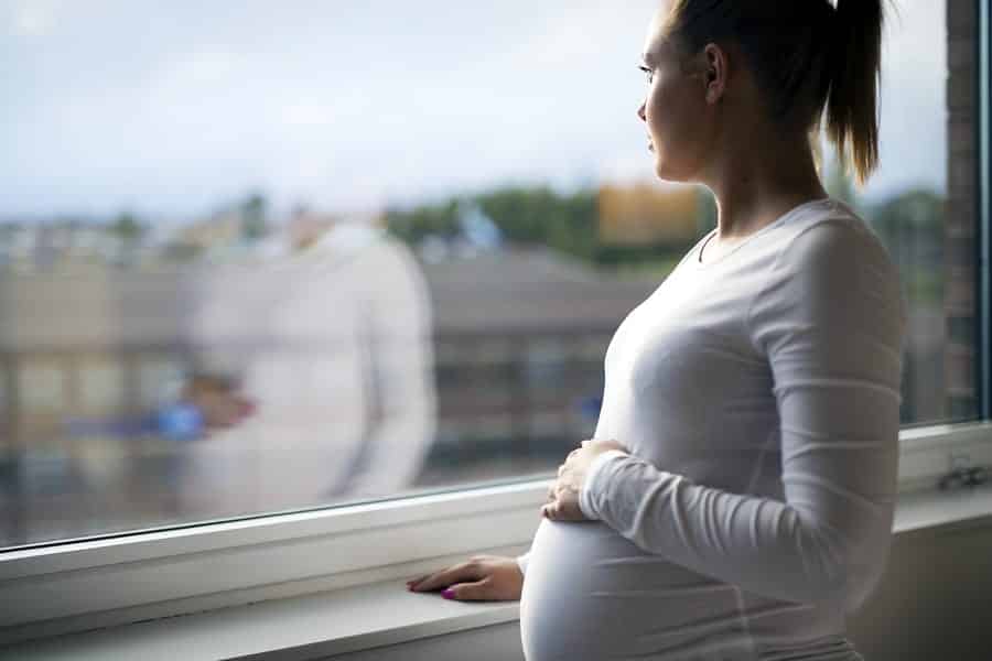 A photo of a thoughtful pregnant woman looking out a window.