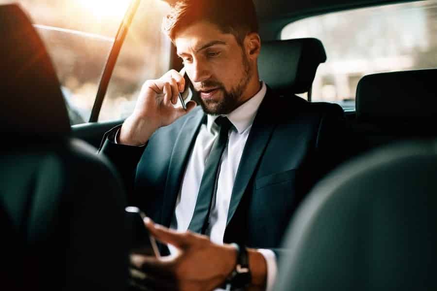 A photo of a man on a business call while riding in a car.