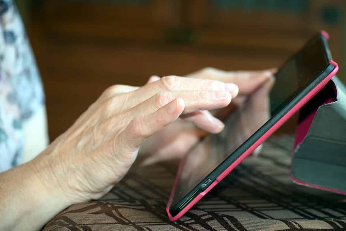 A photo of an older person using a tablet in a pink case.