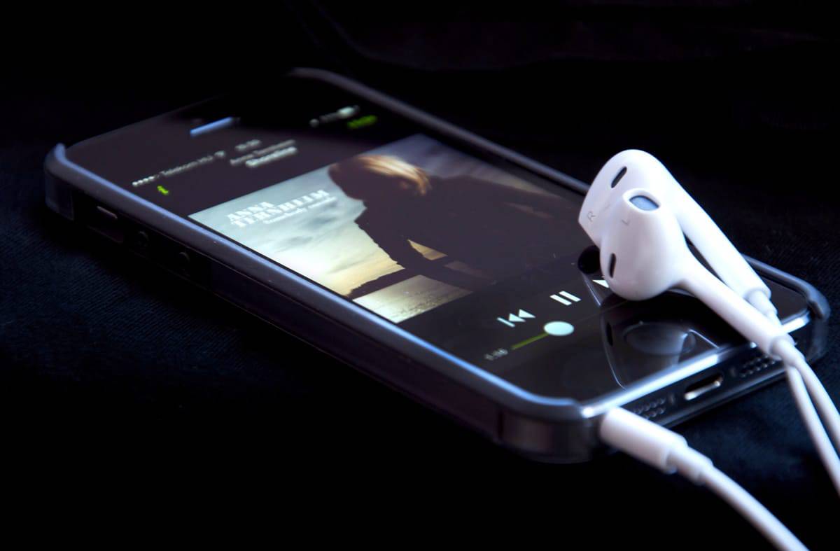 A photo of the music app open on an iPhone and a set of earbuds resting on top.