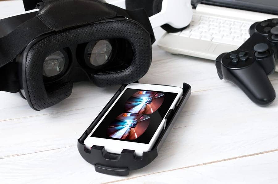 A photo of a VR headset on a table with a smartphone and a video game controller.