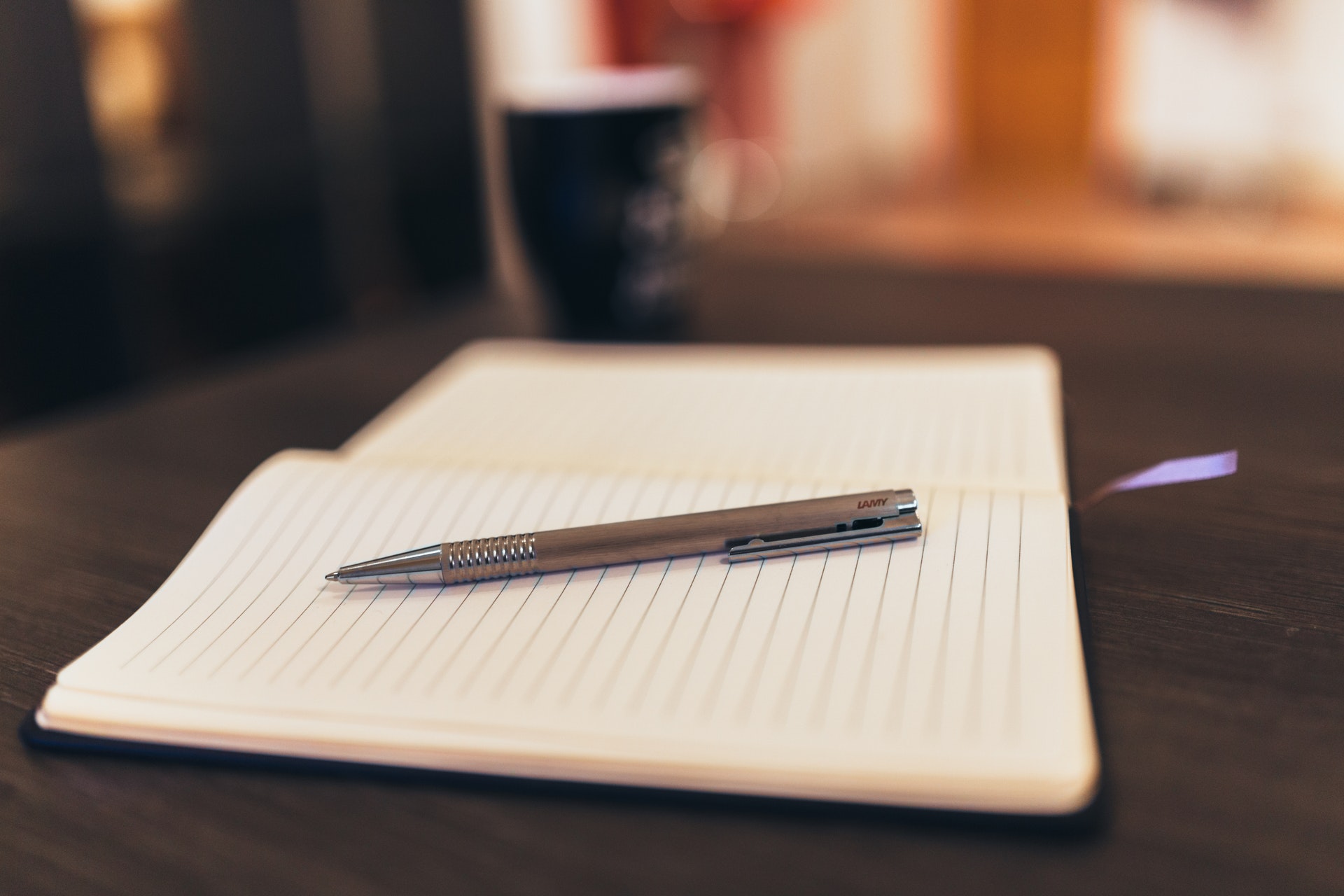 A blank lined notebook and a pen sitting on a desk. 