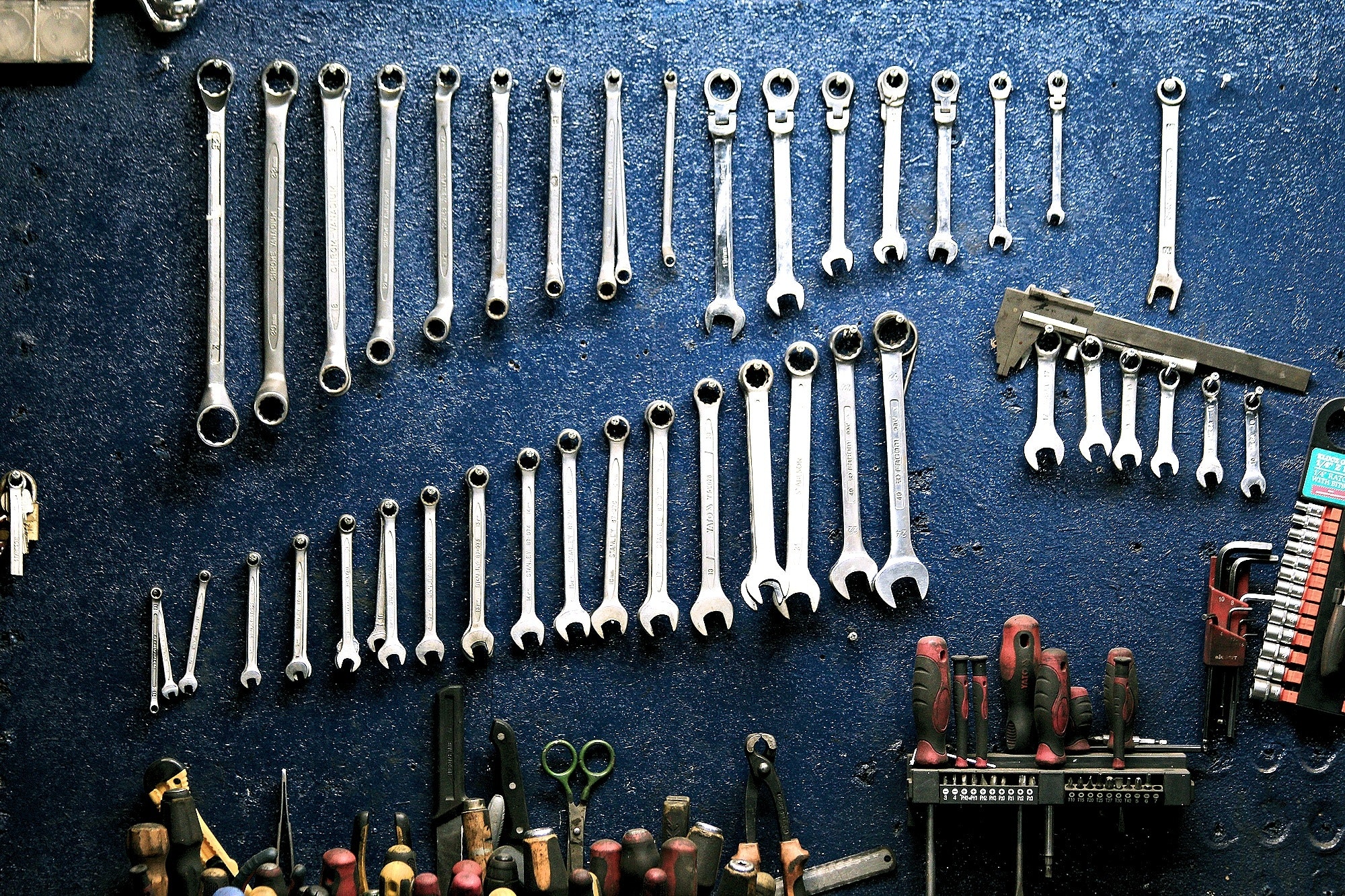 Wrenches and other tools hung up on a blue wall. 